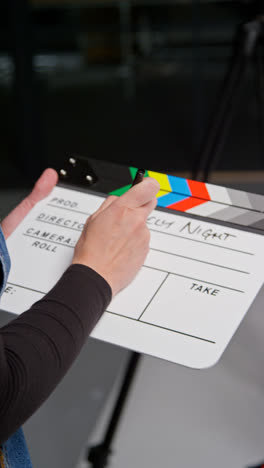 Vertical-Video-Of-Female-Assistant-On-Film-Set-In-Studio-Writing-Movie-Or-Video-Production-Details-Down-On-Clapperboard-Or-Slate